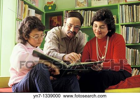 Stock Image - Family of three reading together in the local library. Fotosearch