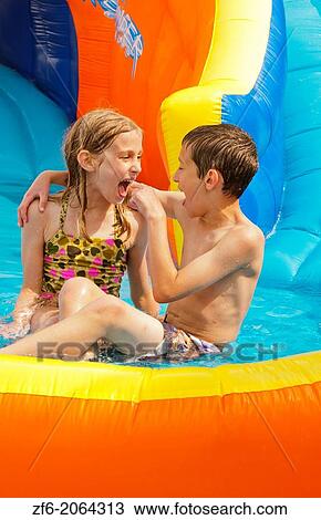 Stock Image - family water slide in back yard at home with water in summer with boy 10 and girl 7 brother and sister playing fun.. Fotosearch