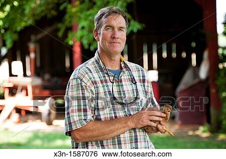 Stock Photograph - Farmer holding chicken on vegetable farm in Queen Anne's County Maryland USA. Fotosearch