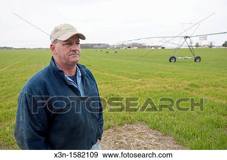 Stock Photo - Farmer standing in planted field next to irrigation system, Salisbury MD. Fotosearch