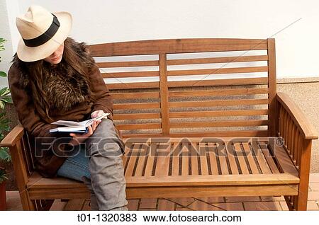 Stock Image - Fashionable girl with Panama hat reading a book outdoors. Fotosearch