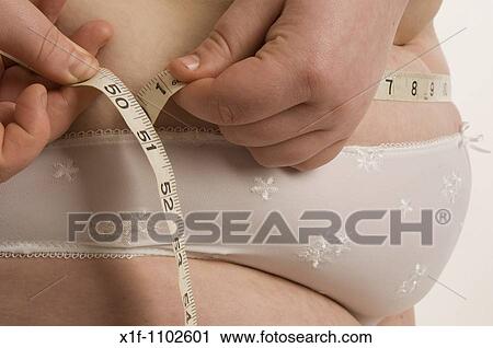 Stock Image - Fat overweight young woman in her underwear measuring her waist. Fotosearch