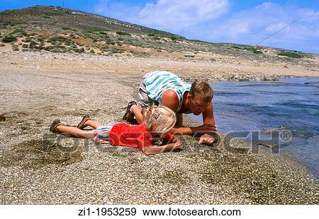 Stock Photo - father and child looking for shells at the beach at Skyros, Greece. Fotosearch