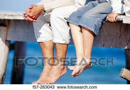 Stock Image - Father and child sitting down in a wooden footbridge over the sea. Fotosearch