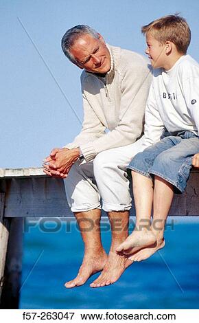 Father and child sitting down in a wooden footbridge over the sea View Large Photo Image Stock Photo - Father and child sitting down in a wooden footbridge over the sea. Fotosearch