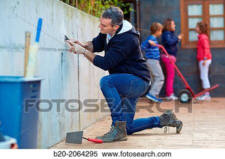 Stock Photography - Father and children doing DIY. Scraping a wall.. Fotosearch