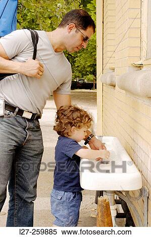 Stock Photography - Father helping his child drink some water from a fountain. Fotosearch