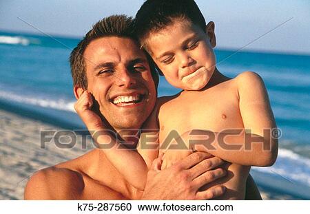 Stock Image - father hugging young son at the beach. Fotosearch