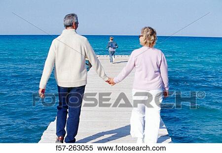 Stock Photography - Father, mother and child walking in a wooden footbridge over the sea. Fotosearch