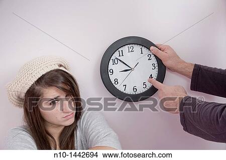 Father pointing to a clock next to his teen daughter View Large Photo Image Picture - Father pointing to a clock next to his teen daughter. Fotosearch