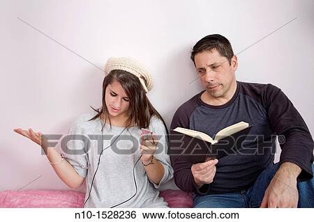 Stock Photograph - Father reading to his teen daughter who is listening to music on her iPod. Fotosearch