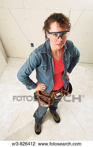 Stock Image - Female construction worker in room with complete wall board installation. Fotosearch