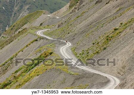 Stock Image - Female cyclist on a winding mountain road, Kyrgyzstan. Fotosearch