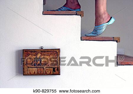 Stock Photography - Female feet of a woman wearing traditional maroccan Babush and climbing up the stairs with a picture of a bible scene hanging on the white washed wall of an old landhouse villa, Gabiano, Piemont, Italy, Europe. Fotosearch