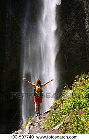 Stock Image - Female hiker basks in the mist of Comet Falls along trail to Van Trump Park in Mt. Rainier National Park, Washington, USA. Fotosearch
