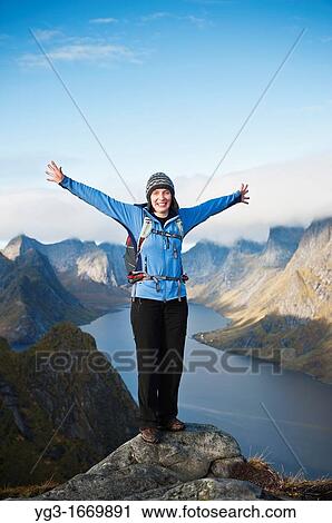 Stock Image - Female hiker enjoys spectacular view over mountains and fjords from Reinebringen, Lofoten islands, Norway. Fotosearch