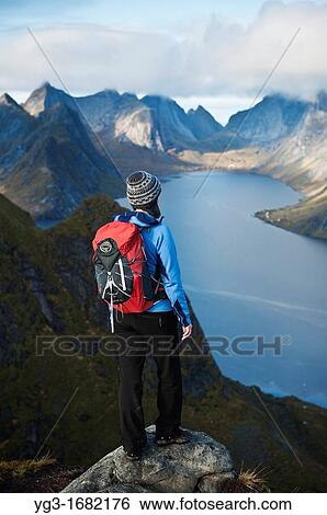 Stock Photograph - Female hiker enjoys spectacular view over mountains and fjords from Reinebringen, Lofoten islands, Norway. Fotosearch