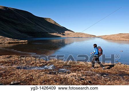 Stock Photo - Female hiker hiking along Llyn Y Fan Fawr in Black Mountian, Brecon Beacons national park, Wales. Fotosearch