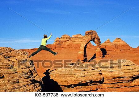 Female hiker leaping from rock to rock with Delicate Arch in background, Arches National Park near Moab, Utah, USA View Large Photo Image Stock Photograph - Female hiker leaping from rock to rock with Delicate Arch in background, Arches National Park near Moab, Utah, USA. Fotosearch