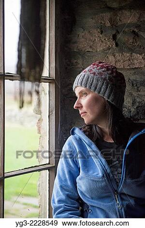 Stock Photo - Female hiker looks out window of Burnmouth Bothy, Rackwick Bay, Hoy, Orkney, Scotland.. Fotosearch