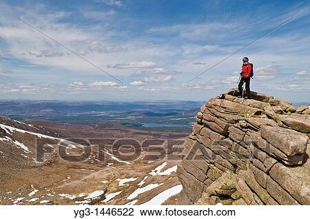 Stock Image - Female hiker stands on cliff near Cairn Gorm in the Cairngorm mountains of Scotland. Fotosearch