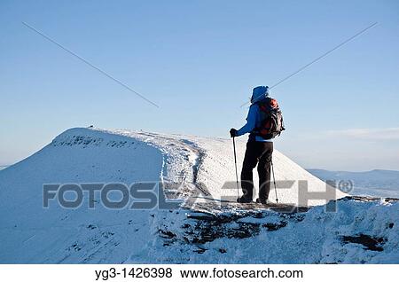 Stock Photo - Female hiker viewing Pen Y Fan from Summit of Corn Du in winter, Brecon Beacons national park, Wales. Fotosearch