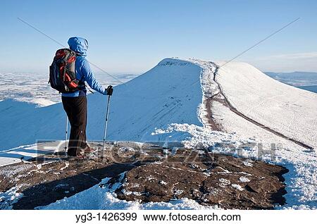Stock Photo - Female hiker viewing Pen Y Fan from Summit of Corn Du in winter, Brecon Beacons national park, Wales. Fotosearch