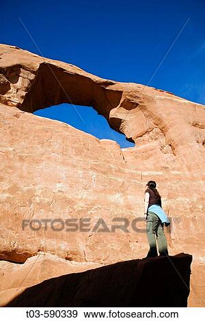 Female hiker viewing Skyline Arch from a large boulder below, Arches National Park, Utah, USA. View Large Photo Image Stock Photo - Female hiker viewing Skyline Arch from a large boulder below, Arches National Park, Utah, USA.. Fotosearch