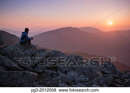 Female hiker watches sunset over mountains from summit of Glyder Fach, Snowdonia national park, Wales. View Large Photo Image Stock Photo - Female hiker watches sunset over mountains from summit of Glyder Fach, Snowdonia national park, Wales.. Fotosearch