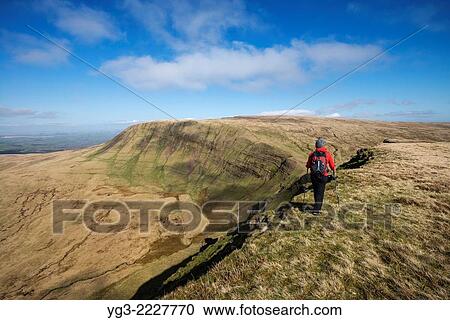 Stock Image - Female hill walker hiking on summit of Picws Du with Fan Brycheiniog in distance, Black Mountain, Brecon Beacons national park, Wales.. Fotosearch