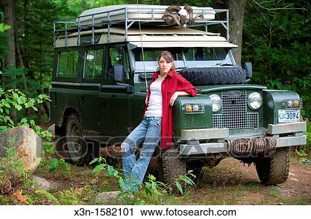 Stock Image - Female model in forest with 1966 Land Rover Series 2A 109 near Lewiston Maine USA. Fotosearch