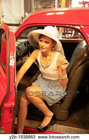 Stock Image - Female model in wide-brimmed white hat by antique red automobile. Fotosearch