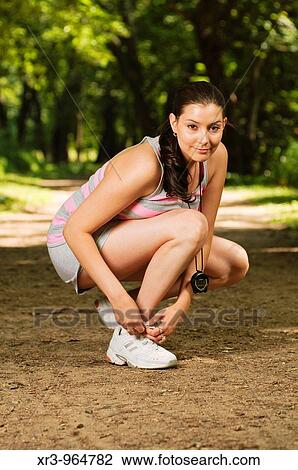 Stock Image - Female runner tying her shoe on wooded urban trail. Fotosearch