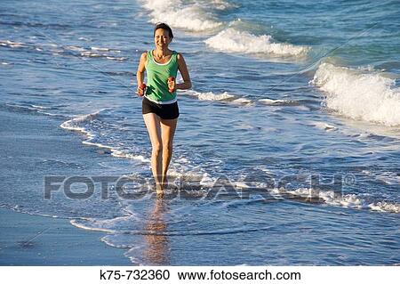 Stock Image - Female running at the beach with weights in hands. Fotosearch