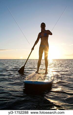 Stock Photo - Female stand-up paddler at sunset at Maui, Hawaii with sunstar. Fotosearch
