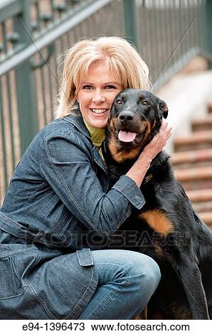 Stock Image - Fifty year old blond woman hugging a Doberman Pinscher on a stairway in a park.. Fotosearch