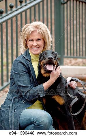 Stock Photo - Fifty year old blond woman hugging a Doberman Pinscher on a stairway in a park.. Fotosearch