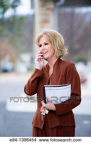 Picture - Fifty year old blond woman in business attire talking on a mobile phone. Fotosearch