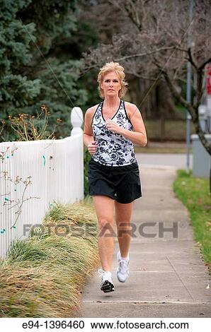 Fifty year old blond woman in fitness attire jogging on a sidewalk in a residential neighborhood View Large Photo Image Stock Image - Fifty year old blond woman in fitness attire jogging on a sidewalk in a residential neighborhood. Fotosearch