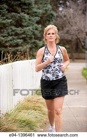 Fifty year old blond woman in fitness attire jogging on a sidewalk in a residential neighborhood View Large Photo Image Stock Image - Fifty year old blond woman in fitness attire jogging on a sidewalk in a residential neighborhood. Fotosearch