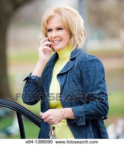 Fifty year old blond woman talking on a mobile phone, outdoors near a car View Large Photo Image Stock Image - Fifty year old blond woman talking on a mobile phone, outdoors near a car. Fotosearch