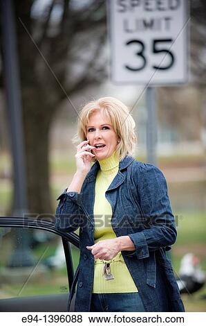Fifty year old blond woman talking on a mobile phone, outdoors near a car View Large Photo Image Stock Photo - Fifty year old blond woman talking on a mobile phone, outdoors near a car. Fotosearch