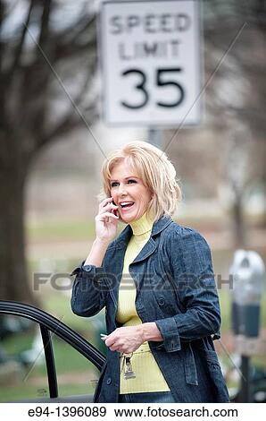 Fifty year old blond woman talking on a mobile phone, outdoors near a car View Large Photo Image Stock Photo - Fifty year old blond woman talking on a mobile phone, outdoors near a car. Fotosearch