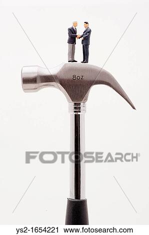 Stock Image - Figurines of businessmen shaking hands on a hammer. Fotosearch