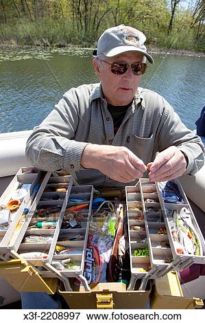 Stock Photo - Fisherman age 70 selecting the proper hook from an array lures in his tackle box. Nisswa Minnesota MN USA.. Fotosearch