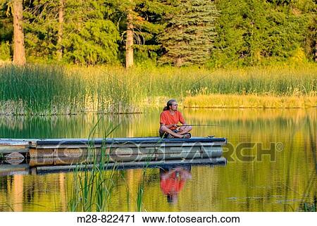 Stock Image - Fisherman in red shirt trying his luck from a dock on Black Pine Lake North Cascades Washington USA. Fotosearch