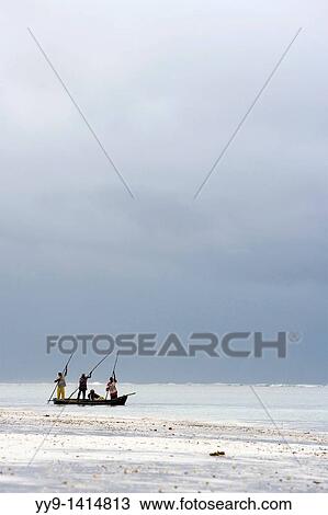 Stock Image - Fisherman poling wooden boat near shoreline - Diani Beach - near Mombasa, Kenya. Fotosearch