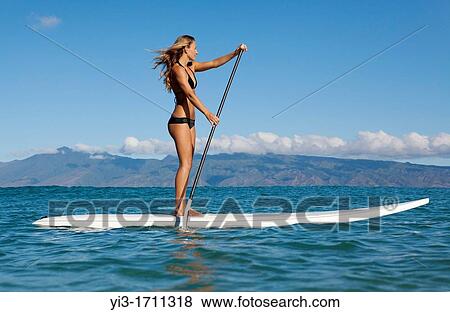Stock Photo - Fit, athletic woman stand up paddles at Napili Bay, Maui, Hawaii with Molokai in the distance. Fotosearch
