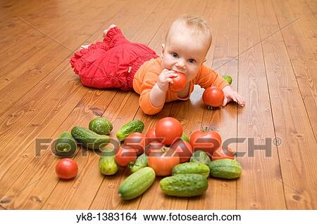 Five month old infant girl lying down on wooden floor eating tomato View Large Photo Image Picture - Five month old infant girl lying down on wooden floor eating tomato. Fotosearch