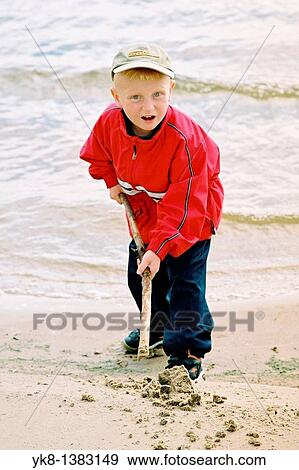Stock Photo - Five Year Old Boy Playing with Wooden Stick on Beach By Water. Fotosearch
